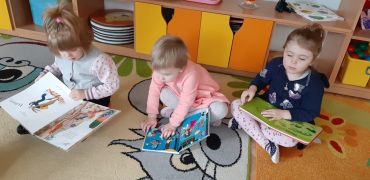 dzieci siedzą na dywanie oglądają książki