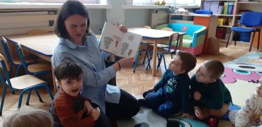 dzieci siedzą na dywanie słuchają książki