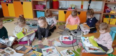 dzieci siedzą na dywanie oglądają książki