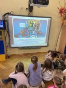 dzieci siedzą na dywanie oglądają prezentację na tablicy multimedialnej