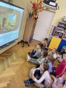 dzieci siedzą na dywanie oglądają prezentację na tablicy multimedialnej