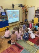 dzieci siedzą na dywanie oglądają prezentację na tablicy multimedialnej