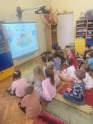 dzieci siedzą na dywanie oglądają prezentację na tablicy multimedialnej