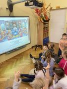 dzieci siedzą na dywanie oglądają prezentację na tablicy multimedialnej