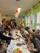 Goście i dzieci siedzą przy stolikach częstują się słodkościami.
