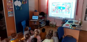 Dzieci siedzą przy tablicy multimedialnej.