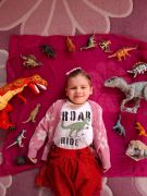 dziecko leży na dywanie z zabawkami dinozaurami
