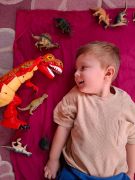 dziecko leży na dywanie z zabawkami dinozaurami