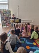 Dzieci siedzą na dywanie, oglądają prezentację multimedialną
