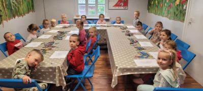 Dzieci przy stolikach wykonują pracę plastyczną.