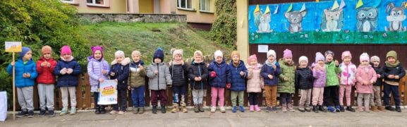 Dzieci pozują z sadzonkami żonkili przed ogródkiem przedszkolnym. 