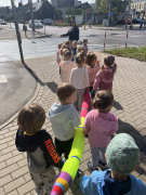 Dzieci trzymając się "węża" stoją z nauczycielką przed skrzyżowaniem.